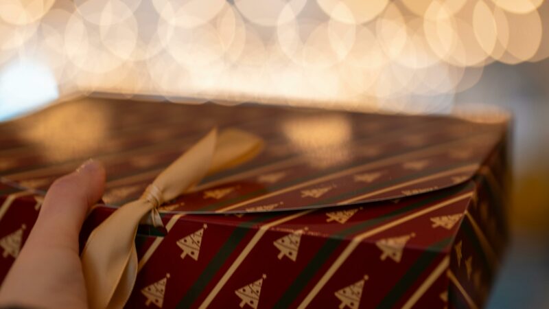 Main tenant un cadeau de Noël dans une ambiance chaleureuse, évoquant les attentes, les liens familiaux et ce qui se rejoue autour du don.